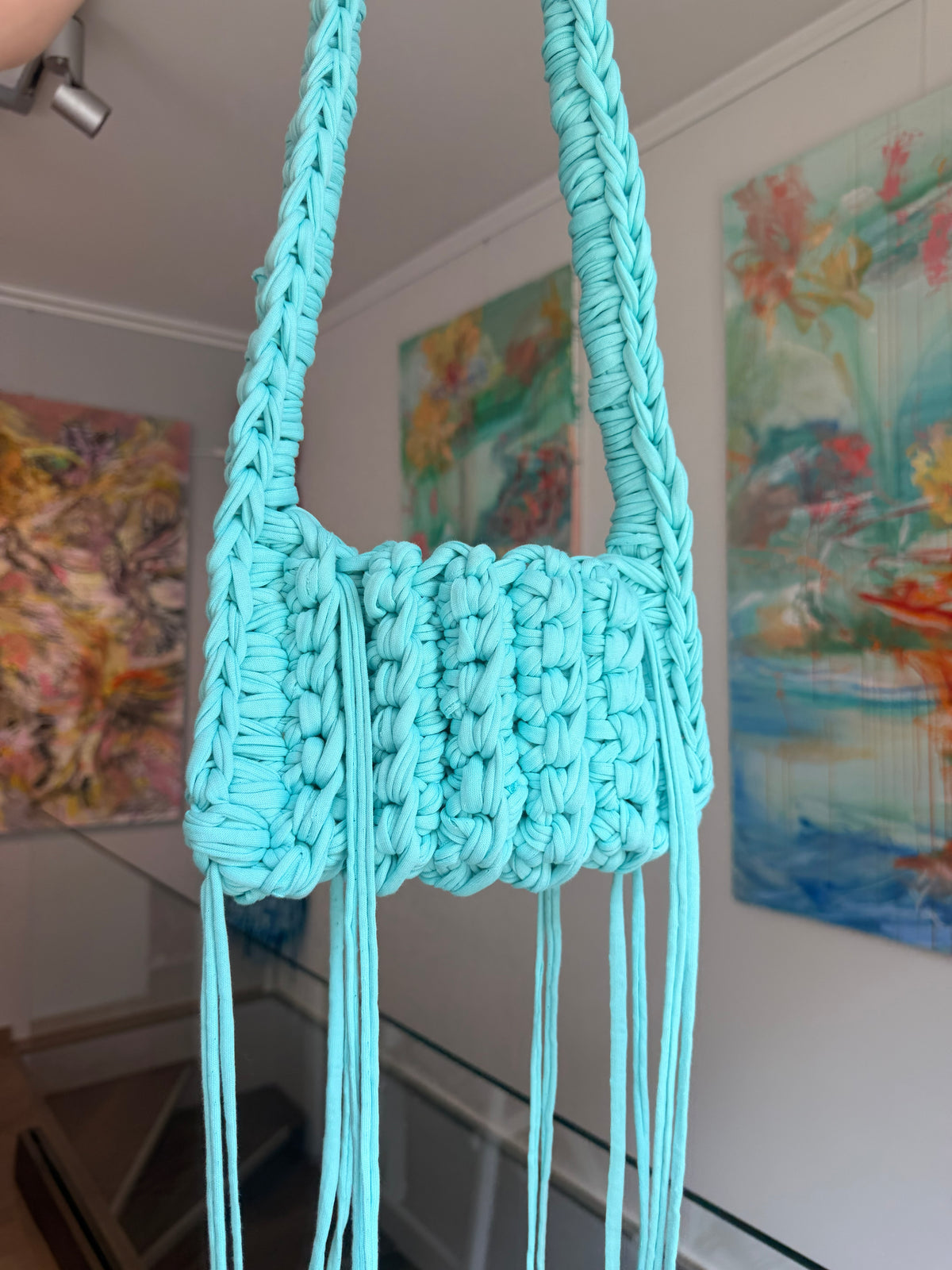 Aqua blue crochet crossbody bag with a long braided strap and a fringe of loose ties