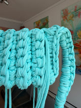 Aqua blue crochet crossbody bag with a long braided strap and a fringe of loose ties