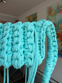 Aqua blue crochet crossbody bag with a long braided strap and a fringe of loose ties