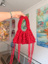 Bright red crochet shoulder bag with a braided top handle and long side ties