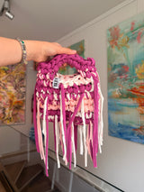 Deep magenta crochet bag banded with blush and cream, with a braided top handle and long fringe