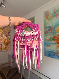 Deep magenta crochet bag banded with blush and cream, with a braided top handle and long fringe