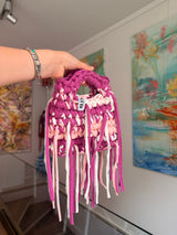 Deep magenta crochet bag banded with blush and cream, with a braided top handle and long fringe