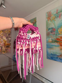 Deep magenta crochet bag banded with blush and cream, with a braided top handle and long fringe