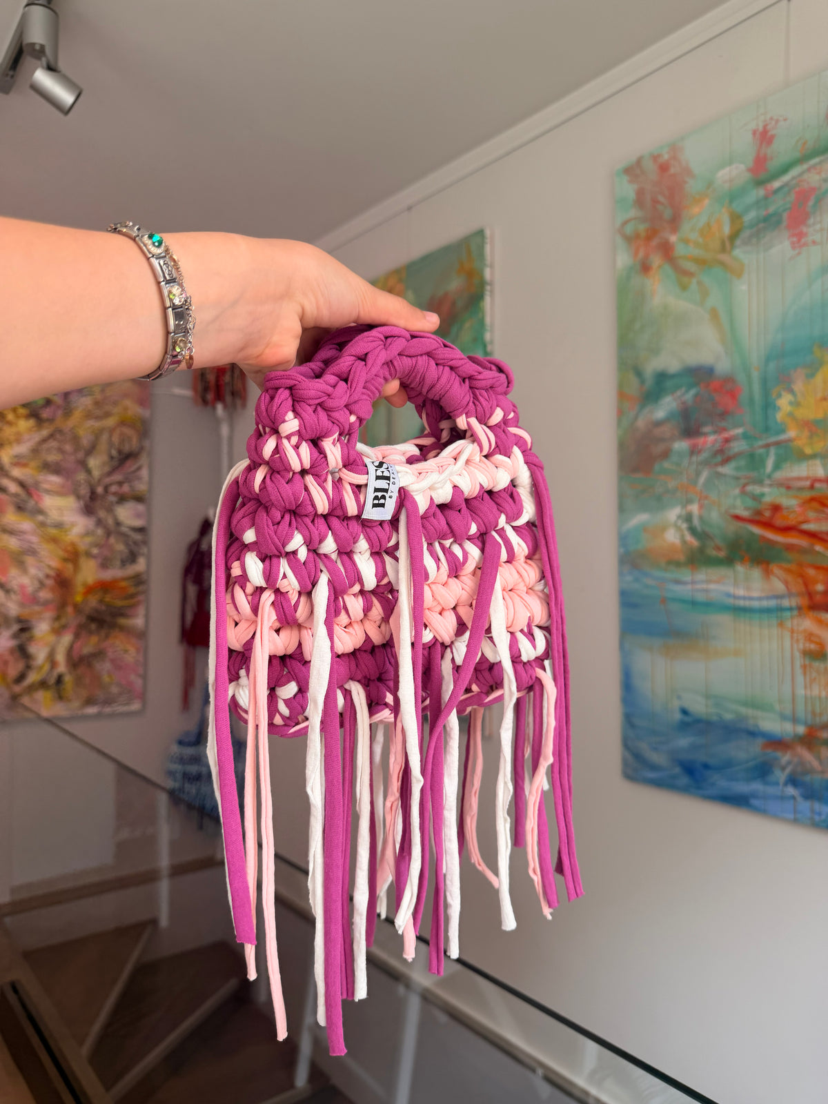 Deep magenta crochet bag banded with blush and cream, with a braided top handle and long fringe