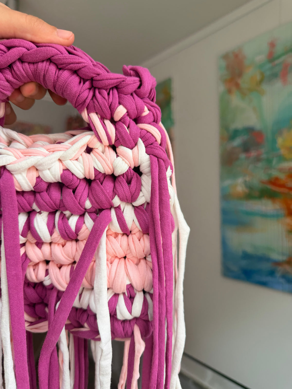 Deep magenta crochet bag banded with blush and cream, with a braided top handle and long fringe