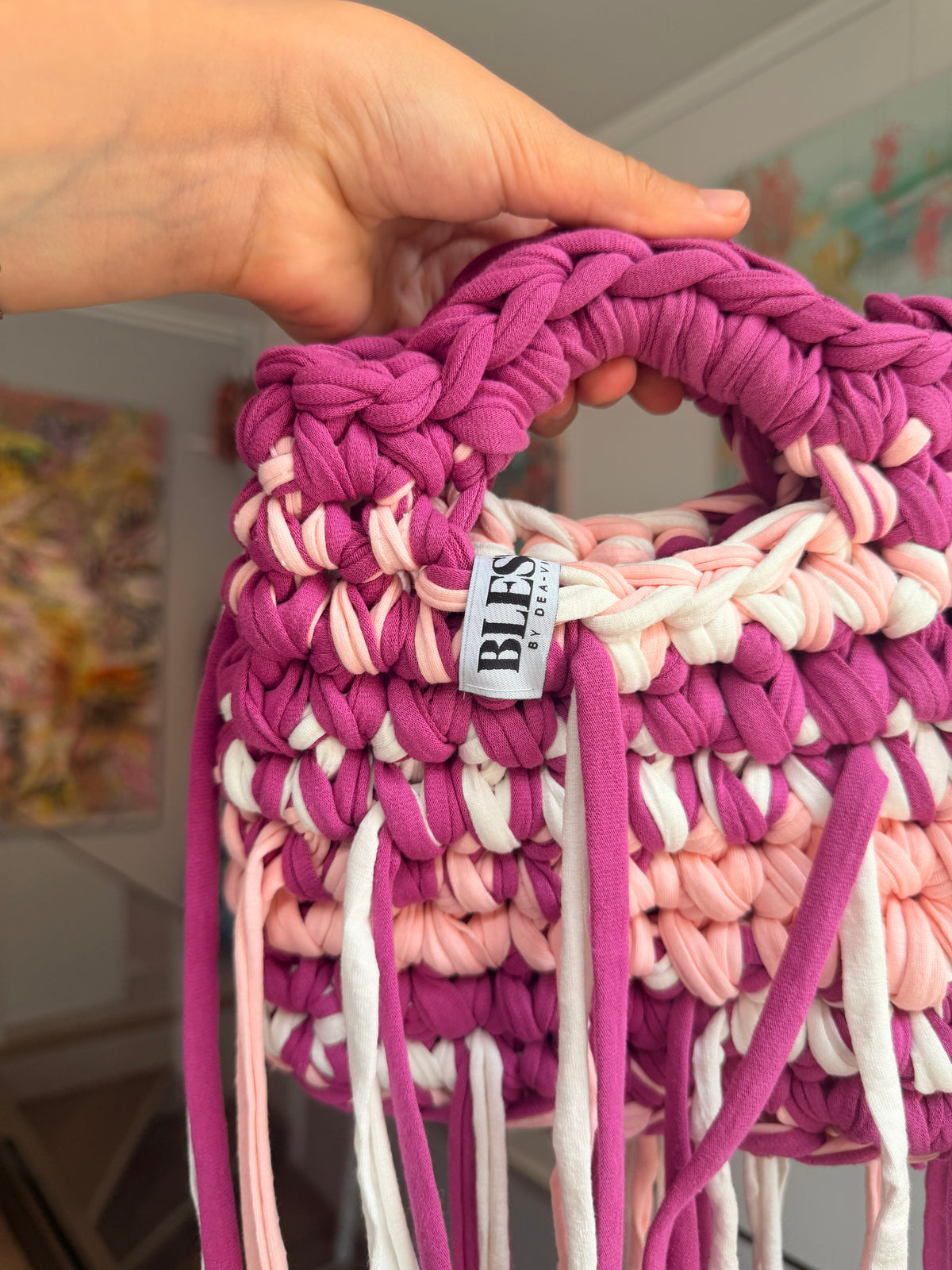 Deep magenta crochet bag banded with blush and cream, with a braided top handle and long fringe