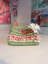 Sage green crochet clutch with a raspberry and cream stripe and a silk flower at the handle