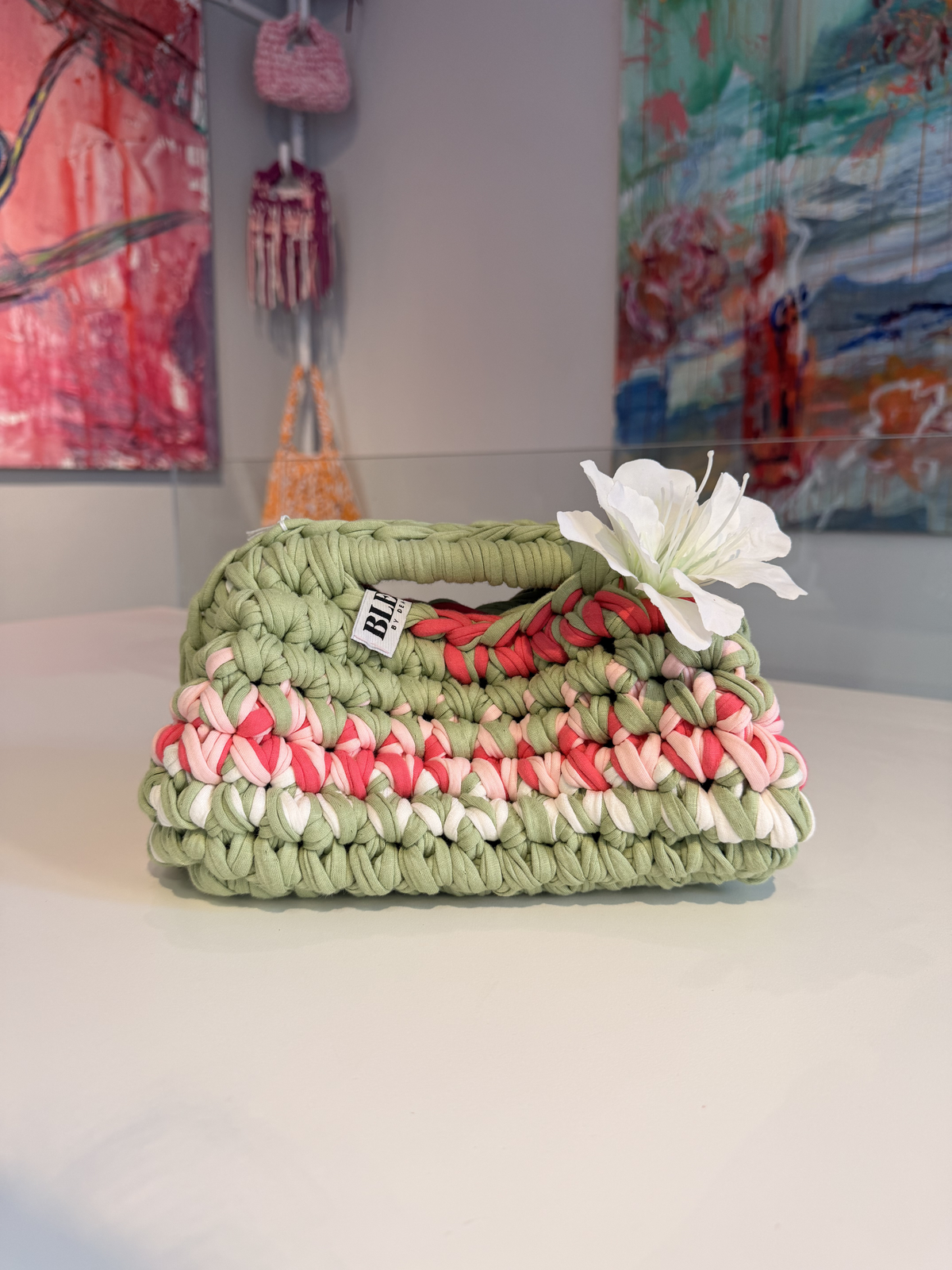 Sage green crochet clutch with a raspberry and cream stripe and a silk flower at the handle